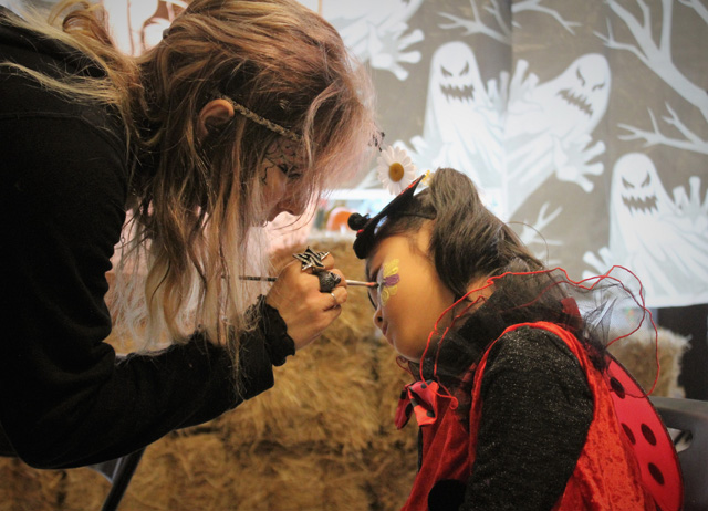 Dawn Miller of Amazing Faces painting a flower on Miso Bang, who dressed as a lady bug for Halloween.