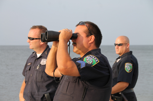 PAUL SQUIRE PHOTO | Riverhead police Sgt. John Vail (center) scans the ocean as Police Officers Christopher Parkin (left) and Rich Freeborn watch on.