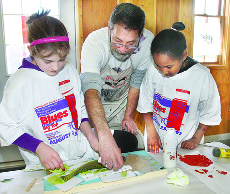 Jack Schwartz of Shoreham, president of the Nature Printing Society, teaches the art of gyotaku, or painting with fish, to Ella Watts Gorman (left), 11, of Southold and Ravyn Elexis Tolliver, 9, of Calverton last Thursday morning at East End Arts Council's carriage house in Riverhead. Gyotaku was developed by Japanese fisherman about 300 years ago to document their catch by rubbing the fish with paint.